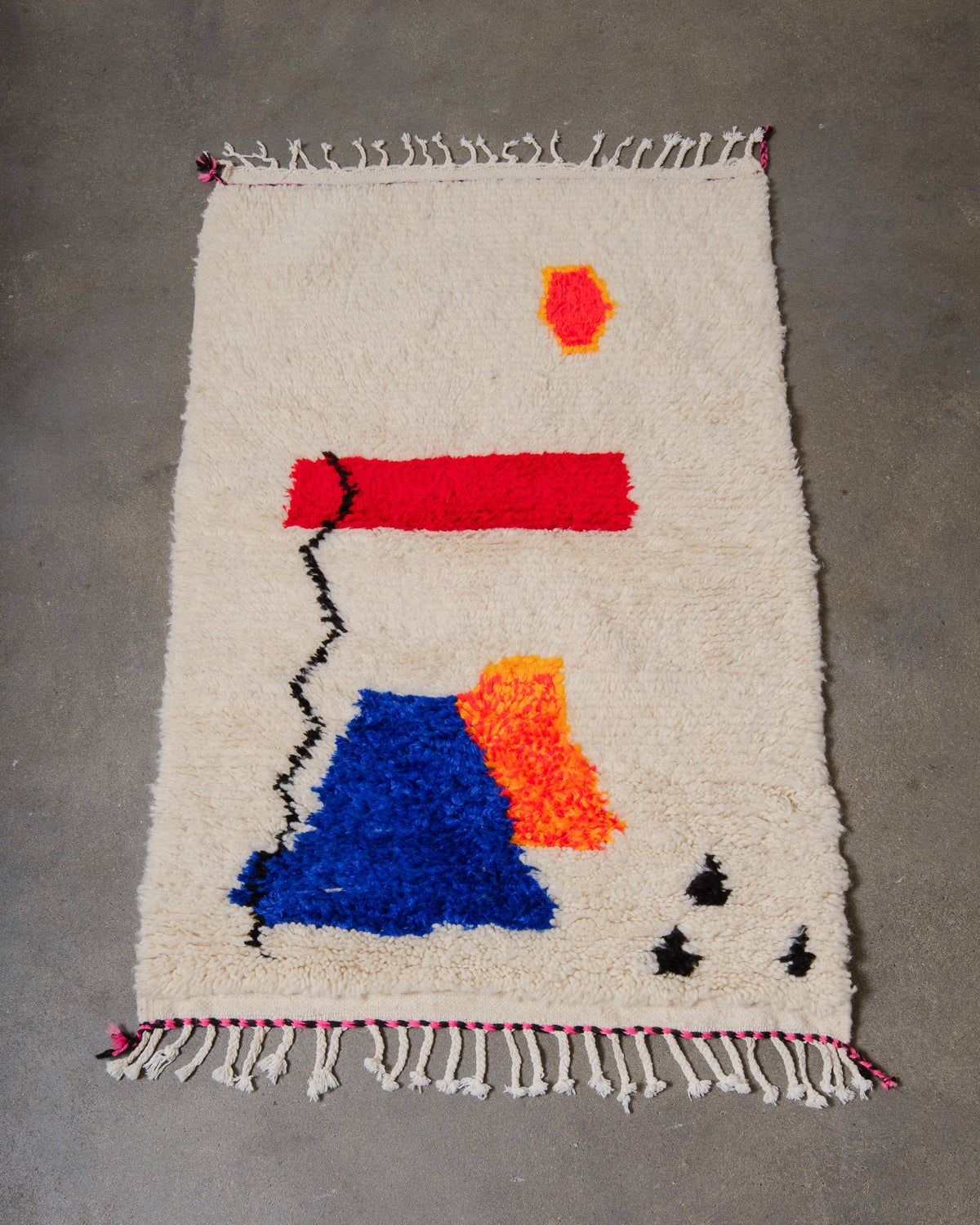 Cream wool Azilal rug with colourful cotton design laying on a concrete floor.